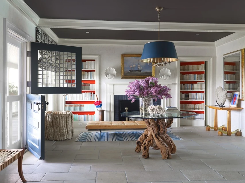 Interior view of a home entryway featuring a driftwood table with flowers, a dutch door, and built-in bookshelves in a bright, stylish space.