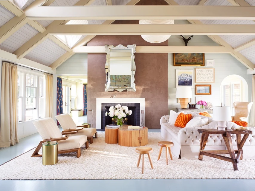 Living room interior with white tufted sofa, wooden tables, and off-white armchairs, bathed in natural light from the window.