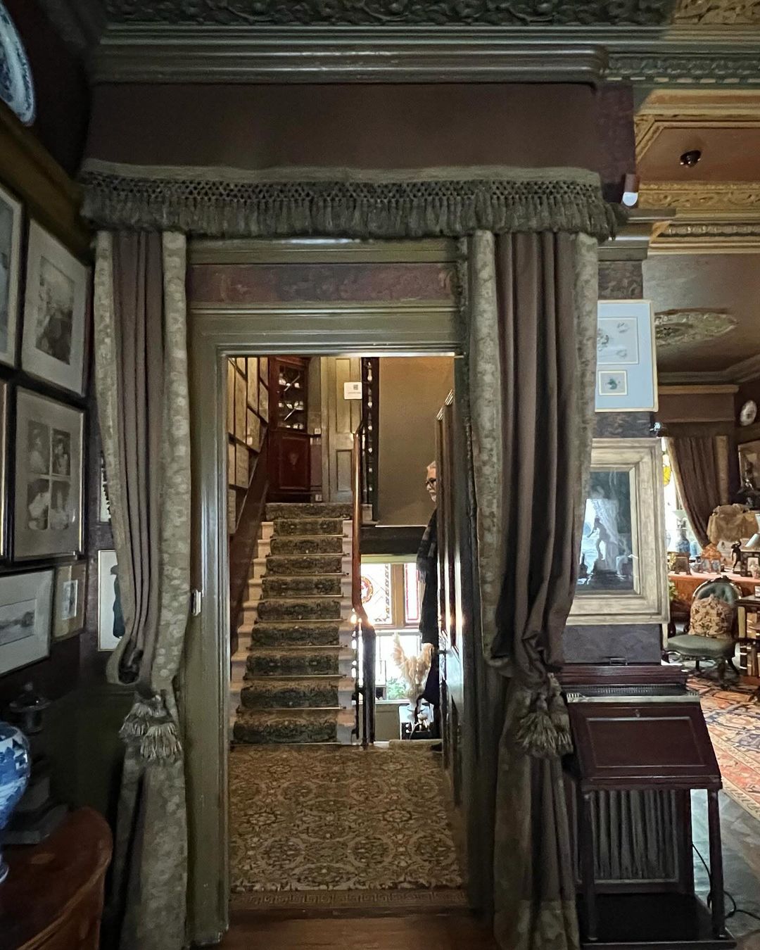 Elegant home interior featuring a hallway with a staircase, ornate decor, curtains, and vintage-style furnishings, creating a warm, inviting atmosphere.
