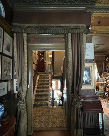 Elegant home interior featuring a hallway with a staircase, ornate decor, curtains, and vintage-style furnishings, creating a warm, inviting atmosphere.