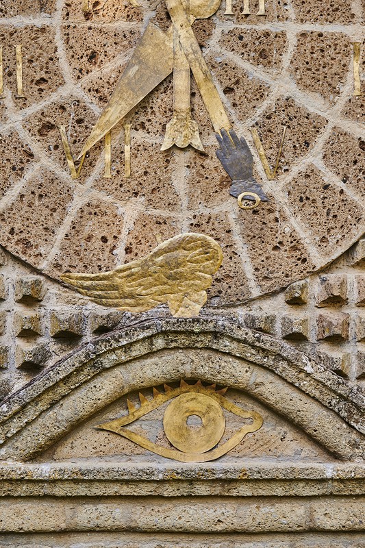 Ancient stone sundial carving featuring hand, wing, and eye symbols on a textured wall, conveying time and history with neutral tones.