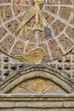 Ancient stone sundial carving featuring hand, wing, and eye symbols on a textured wall, conveying time and history with neutral tones.