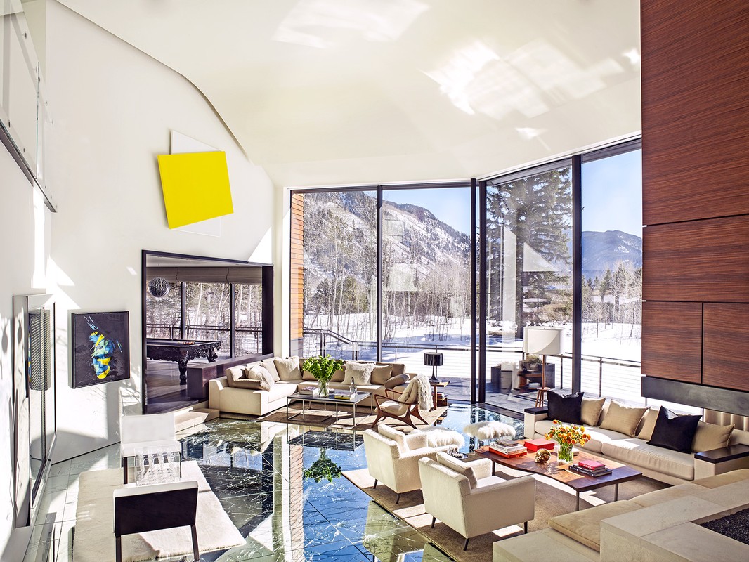 Bright and open living room with marble floor, modern furniture, and large windows showcasing snowy mountain views; artwork on walls.