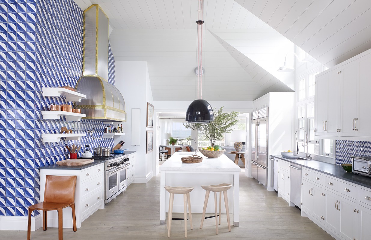 Bright modern kitchen with blue patterned wall tiles, white cabinetry, and a central island with stools under a black pendant lamp.