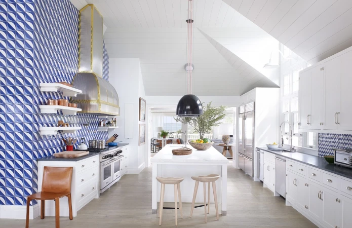 Bright modern kitchen with blue patterned wall tiles, white cabinetry, and a central island with stools under a black pendant lamp.