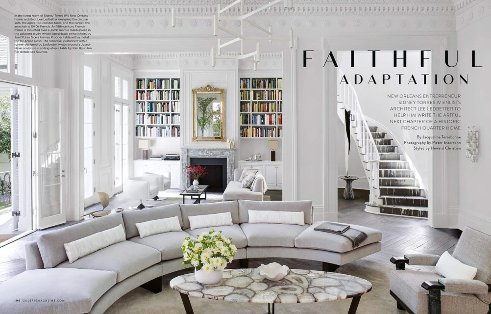 Bright, stylish living room interior features a curved sectional sofa, marble fireplace, bookshelves, and staircase in a New Orleans home.