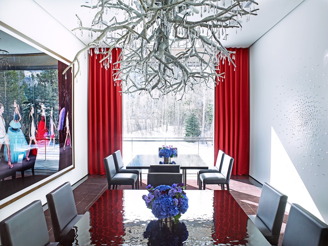 Formal dining room featuring long reflective dining table, gray chairs, unique chandelier, and a large framed fashion photograph.