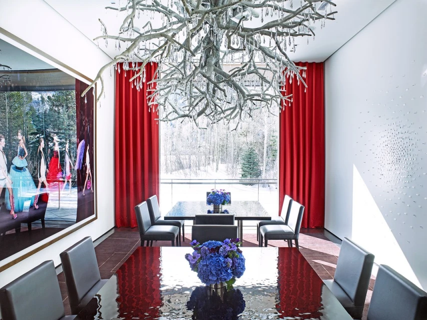 Formal dining room featuring long reflective dining table, gray chairs, unique chandelier, and a large framed fashion photograph.