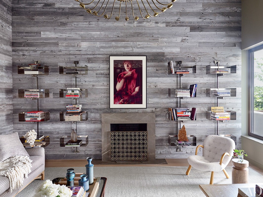 Living room interior with gray wood paneling, bookshelves, a fireplace, area rug, artwork, and a white upholstered chair.
