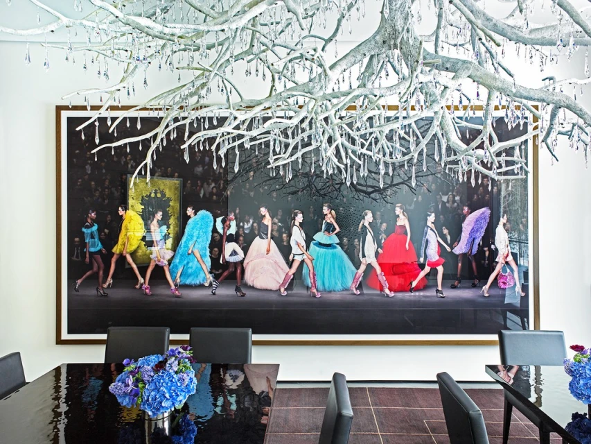 Fashion photography of models on a runway, framed in a modern interior with chandelier above a reflective table and contemporary decor.