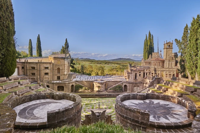 Detailed view of theatrical architectural landscape with amphitheater and buildings, set against backdrop of trees and blue sky.