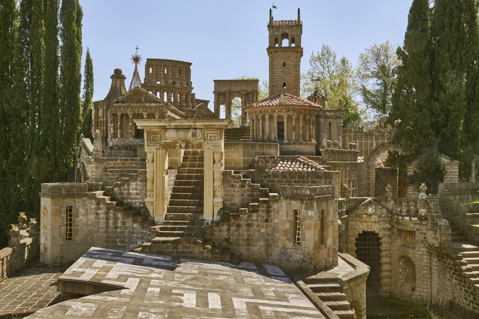Architectural view of the partially ruined, stone-constructed Scarzuola in Umbria, Italy, with towers and staircases under a blue sky.
