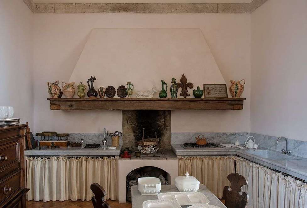 Rustic kitchen interior with farmhouse sink, wooden furniture, antique jugs, vintage cookware, marble countertops and natural light.