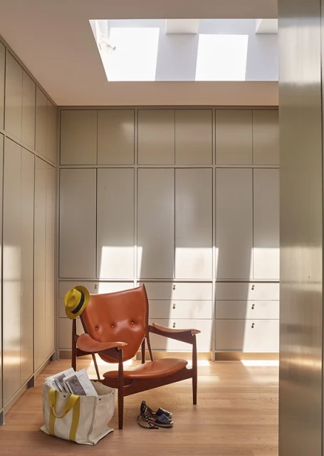 Interior view of a modern room with a leather chair, hat, tote bag with newspapers, and shoes, illuminated by natural light from a skylight.