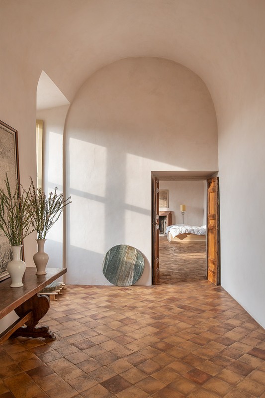 Indoor view of a Mediterranean-style home showcasing terracotta tile floors, an archway, a wooden console table, and neutral color palette.