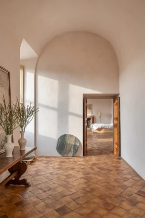 Indoor view of a Mediterranean-style home showcasing terracotta tile floors, an archway, a wooden console table, and neutral color palette.