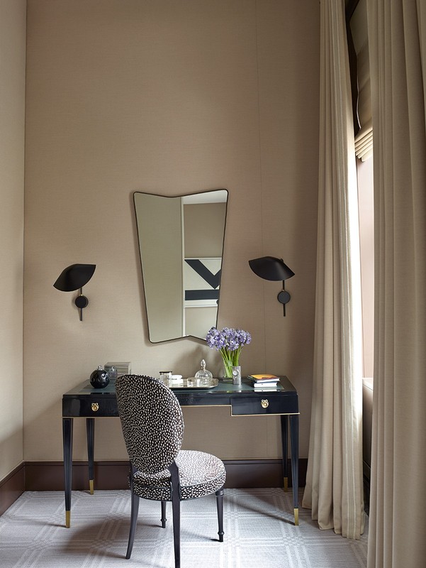 Interior of a room featuring a vanity desk with a mirror, chair, table lamps, flowers, and various decorative objects.