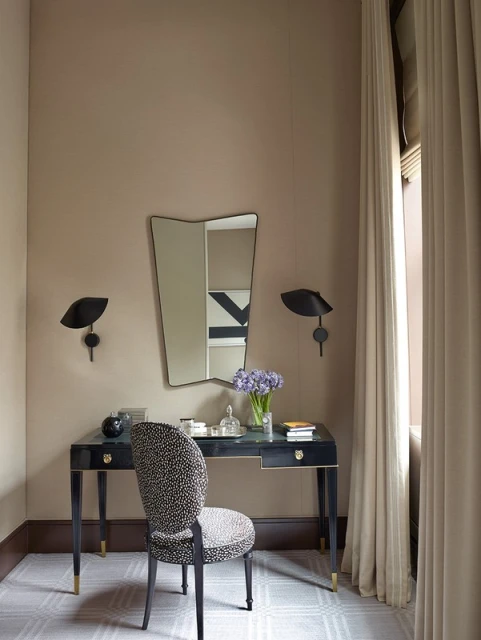 Interior of a room featuring a vanity desk with a mirror, chair, table lamps, flowers, and various decorative objects.