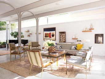 Bright living room interior with a low sofa, armchairs, arched steel beams, and white painted brick walls photographed by Pieter Estersohn.