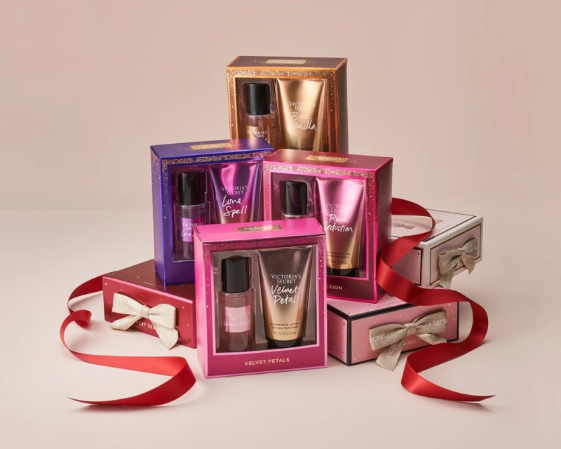 Various Victoria's Secret fragrance lotion and body spray sets stacked with a red ribbon on a pink background, product-focused beauty shot.