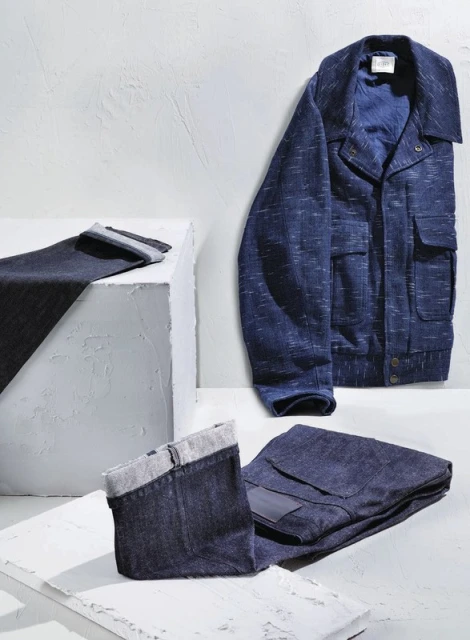 Studio shot of a blue jacket and folded blue denim pants on white geometric surfaces, creating a modern fashion product presentation.
