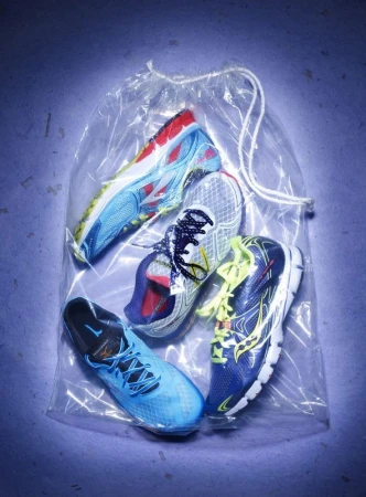 Studio shot of four pairs of colorful running shoes in a clear plastic drawstring bag, blue lighting, and a textured background.