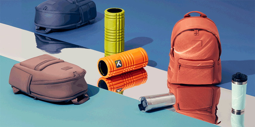 Still life featuring backpacks in orange, purple, and brown, a green and orange massage roller, and a steel drinking bottle against a blue background.