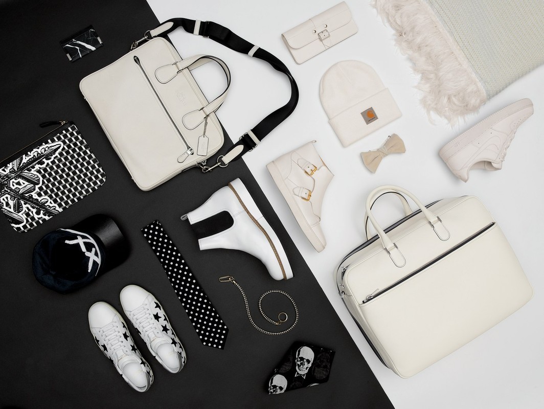 Flat lay of white and black fashion accessories, bags, and shoes arranged on a split-tone background.