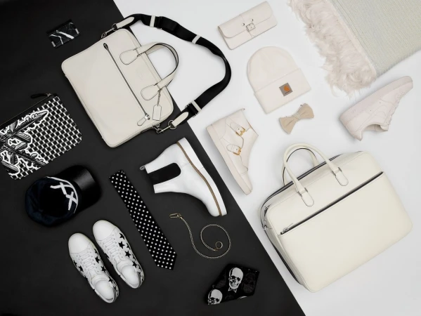 Flat lay of white and black fashion accessories, bags, and shoes arranged on a split-tone background.