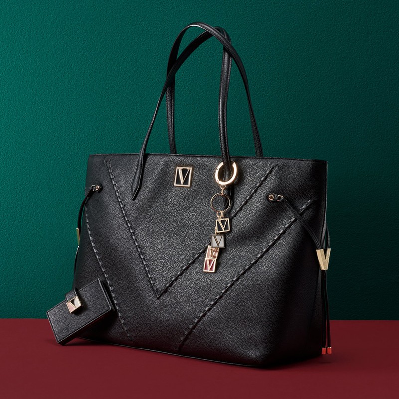 Black leather tote bag with gold logo and keychain on a red surface against a green backdrop. Fashionable handbag with elegant details.