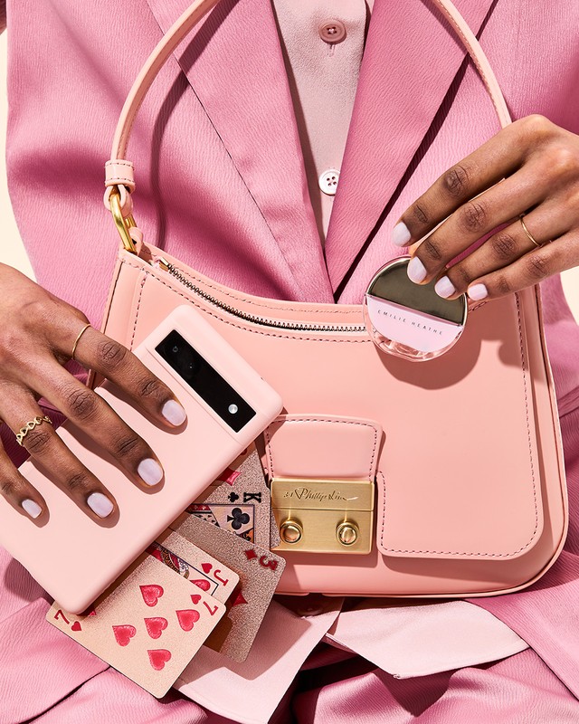 Pink handbag and smartphone held in hand with playing cards spilling out, styled with matching pink jacket and accessories.