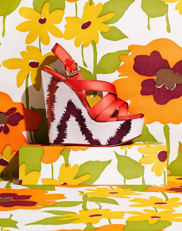 Platform sandal with red straps on a patterned surface featuring retro flower designs in yellow, orange, and green colors.
