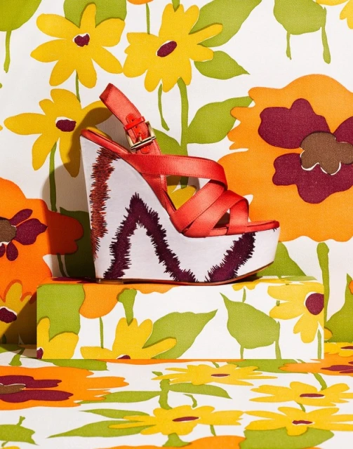 Platform sandal with red straps on a patterned surface featuring retro flower designs in yellow, orange, and green colors.