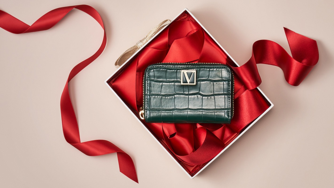 A green wallet in a white gift box with a red ribbon on a neutral background, product photography with fashion and gifting elements.