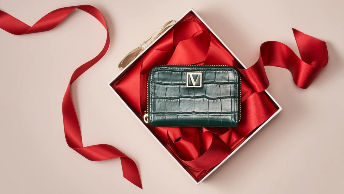 A green wallet in a white gift box with a red ribbon on a neutral background, product photography with fashion and gifting elements.