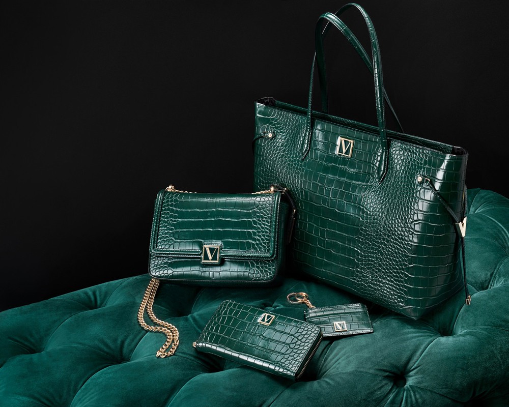 Emerald green leather-look handbags and accessories arranged on a matching tufted cushion against a dark background.