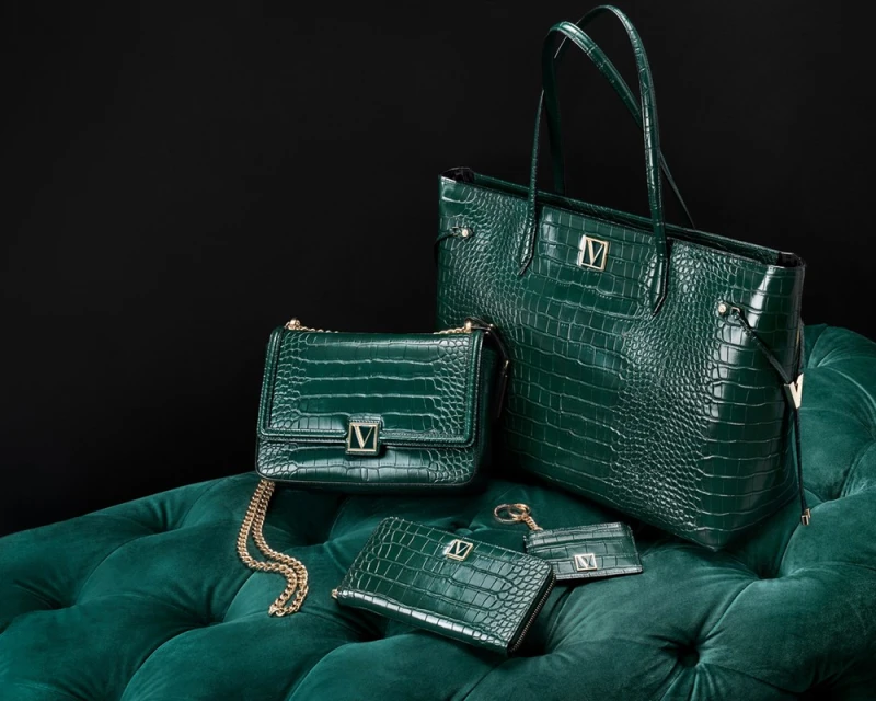 Emerald green leather-look handbags and accessories arranged on a matching tufted cushion against a dark background.