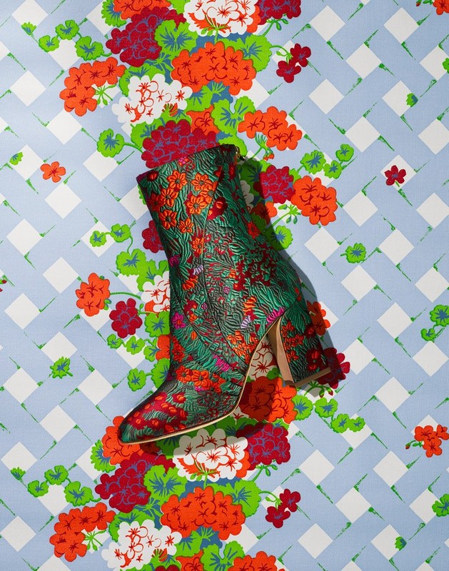 Elevated product shot of a green floral-patterned boot with a heel on a floral and geometric patterned background.