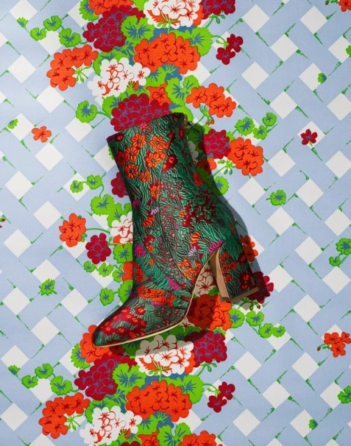 Elevated product shot of a green floral-patterned boot with a heel on a floral and geometric patterned background.
