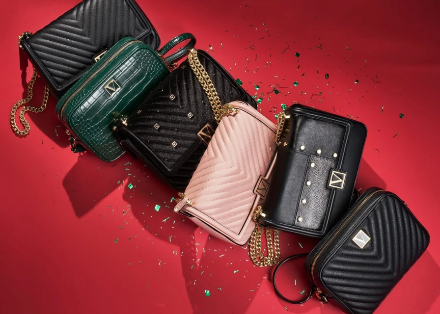 Collection of fashionable handbags in black, green, and pink hues arranged on a red background, highlighted with scattered glitter.
