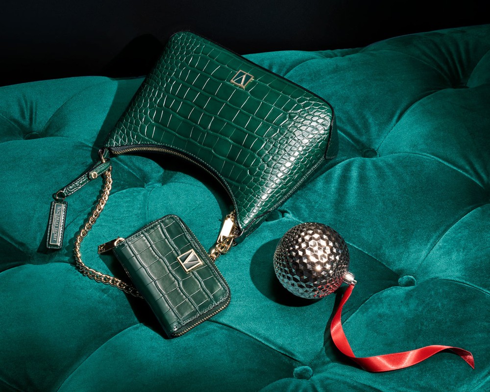 Elegant green crocodile-patterned handbag and wallet with gold chain, paired with a decorative sphere on a tufted velvet surface.