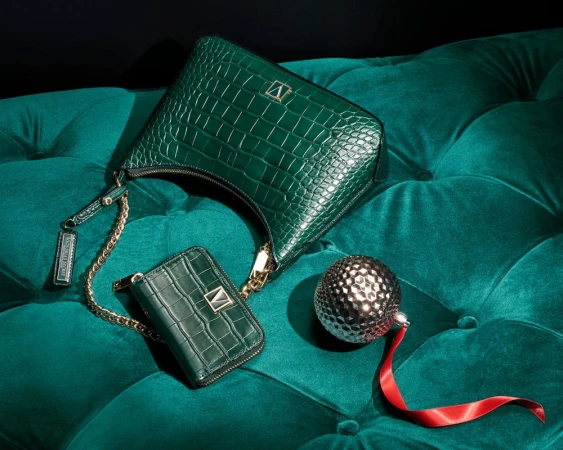 Elegant green crocodile-patterned handbag and wallet with gold chain, paired with a decorative sphere on a tufted velvet surface.