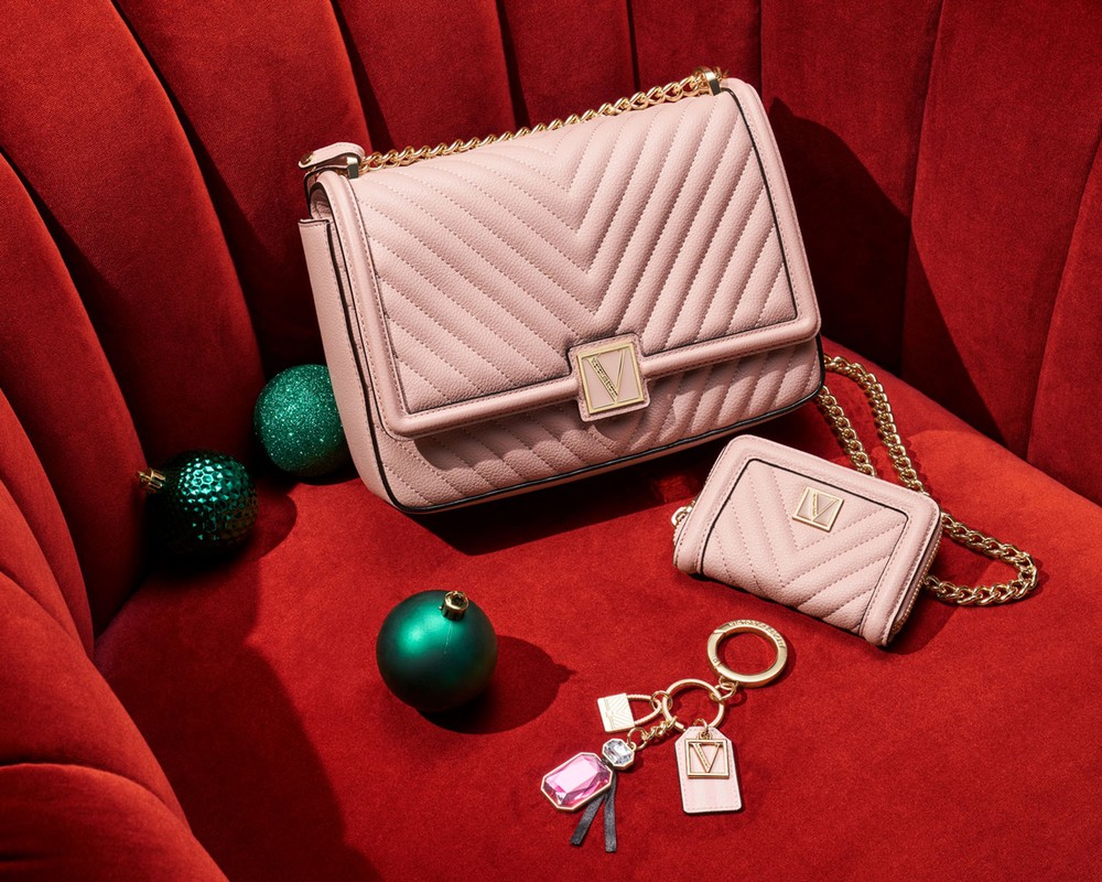 Pale pink chevron shoulder bag with gold chain strap, matching wallet, and keychain on a red velvet surface next to ornaments.