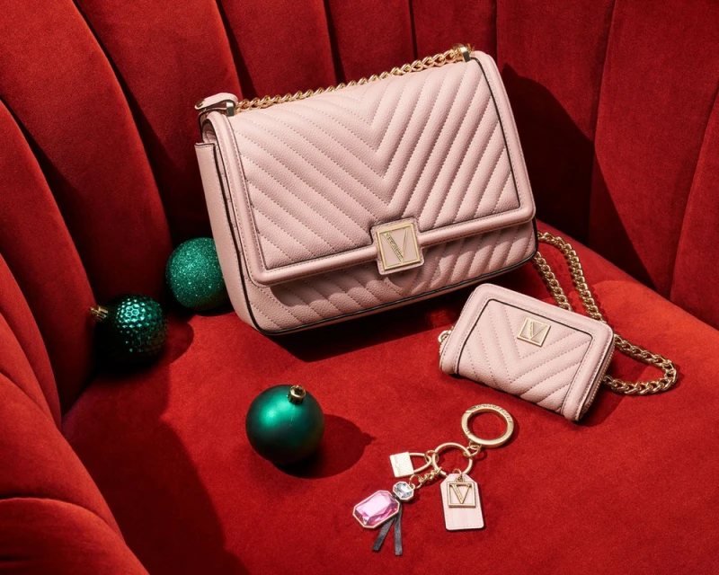 Pale pink chevron shoulder bag with gold chain strap, matching wallet, and keychain on a red velvet surface next to ornaments.