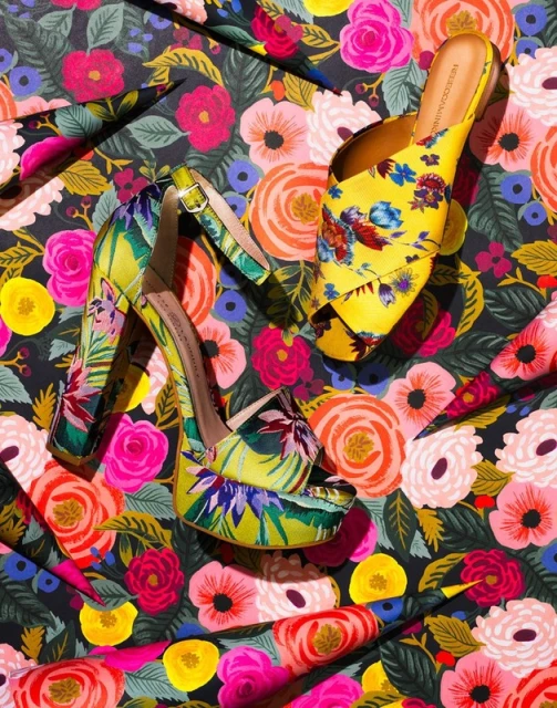 High-heeled platform sandals and open-toe mules with bright floral pattern designs are displayed on a colorful floral background.