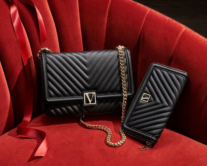 Chevron quilted black leather crossbody bag with a gold chain strap and a zip wallet on a red velvet armchair.