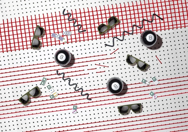 Arrangement of sunglasses, billiard balls, and dominoes on a white surface with red lines and black dots in a studio setting.