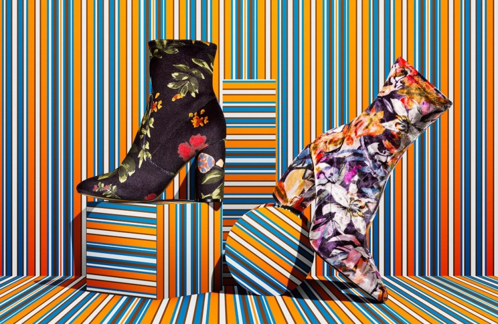 Floral ankle boots displayed on striped blocks against a striped backdrop, creating a vibrant, patterned fashion product shot.