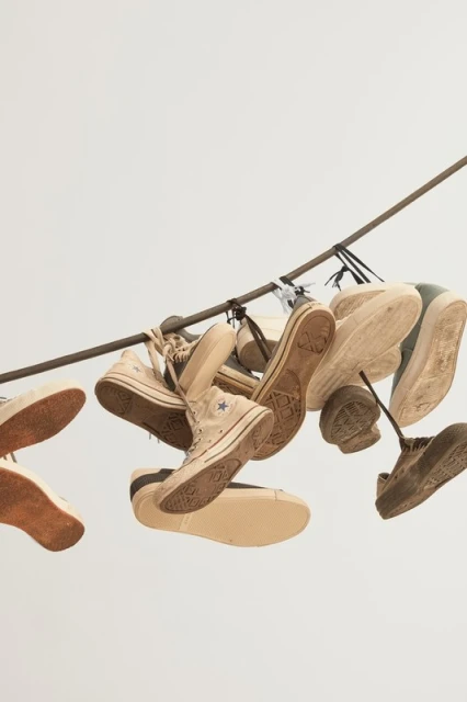 Group of worn canvas sneakers hanging from a rusty metal rod, showcasing worn soles and beige, tan, and brown color palette in studio.
