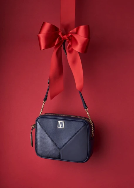 Elegant navy blue cross-body purse with a prominent V logo, suspended from a red satin ribbon against a matching red backdrop.